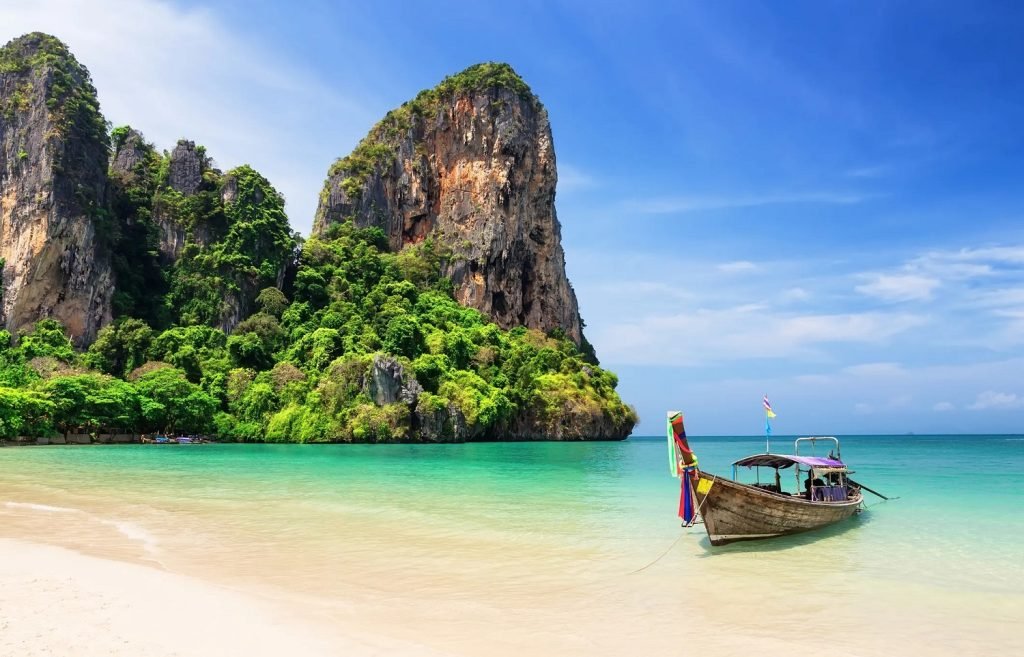 Traditional Thai longtail boat anchored in clear blue water near a white sand beach and green limestone cliffs